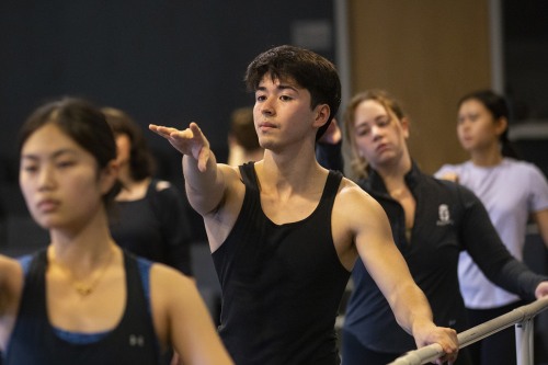 Dancers hold a horizontal bar while stretching their left arms forward