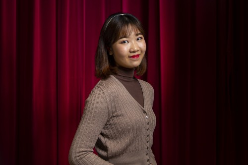 Glory smiles while standing in front of a red theater curtain