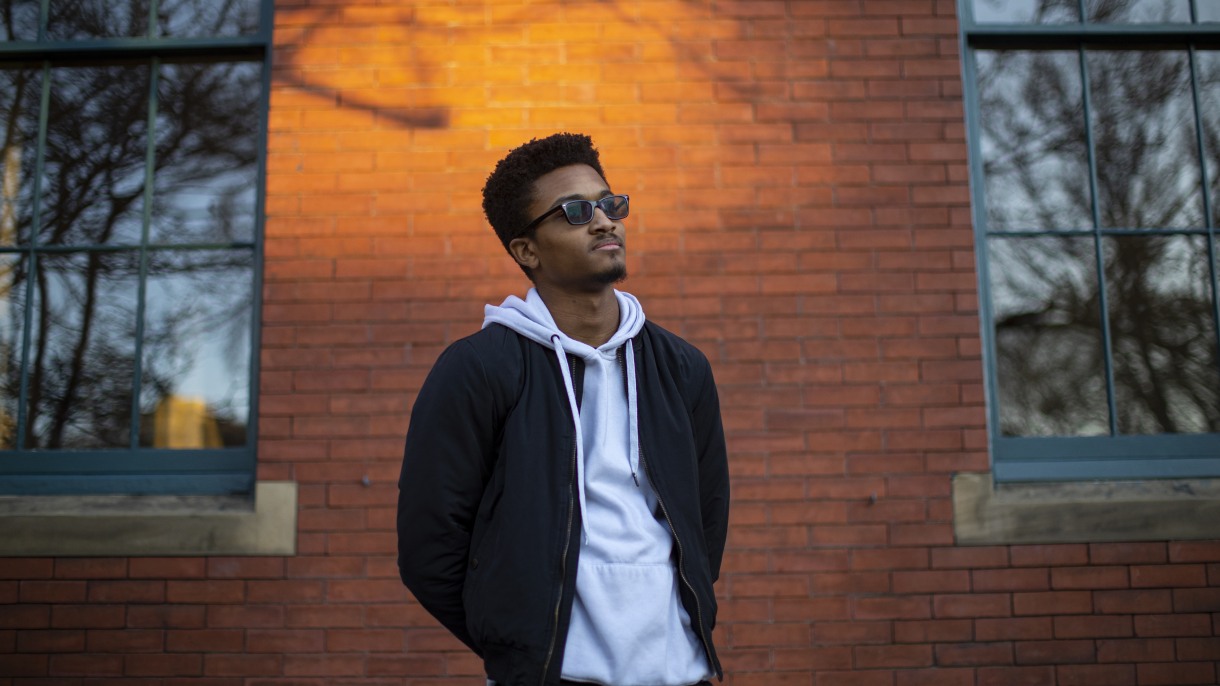 Alejandro stands in front of a brick building, in sunglasses